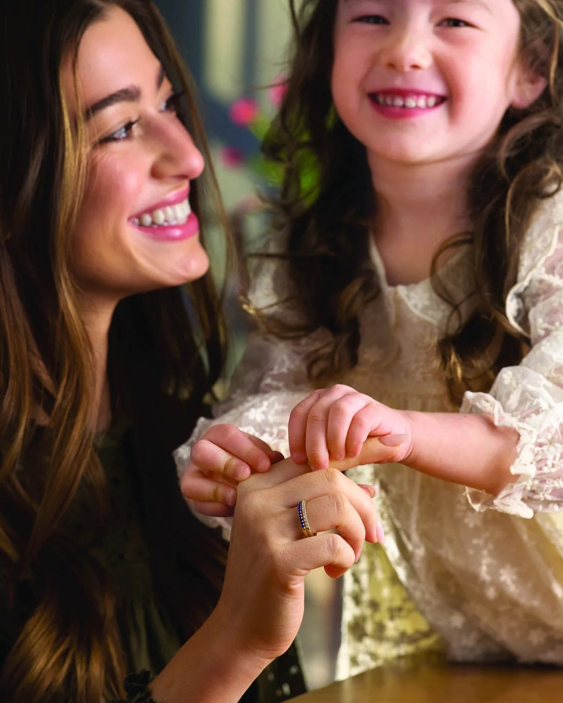 Woman and young girl sitting together, smiling and holding hands.